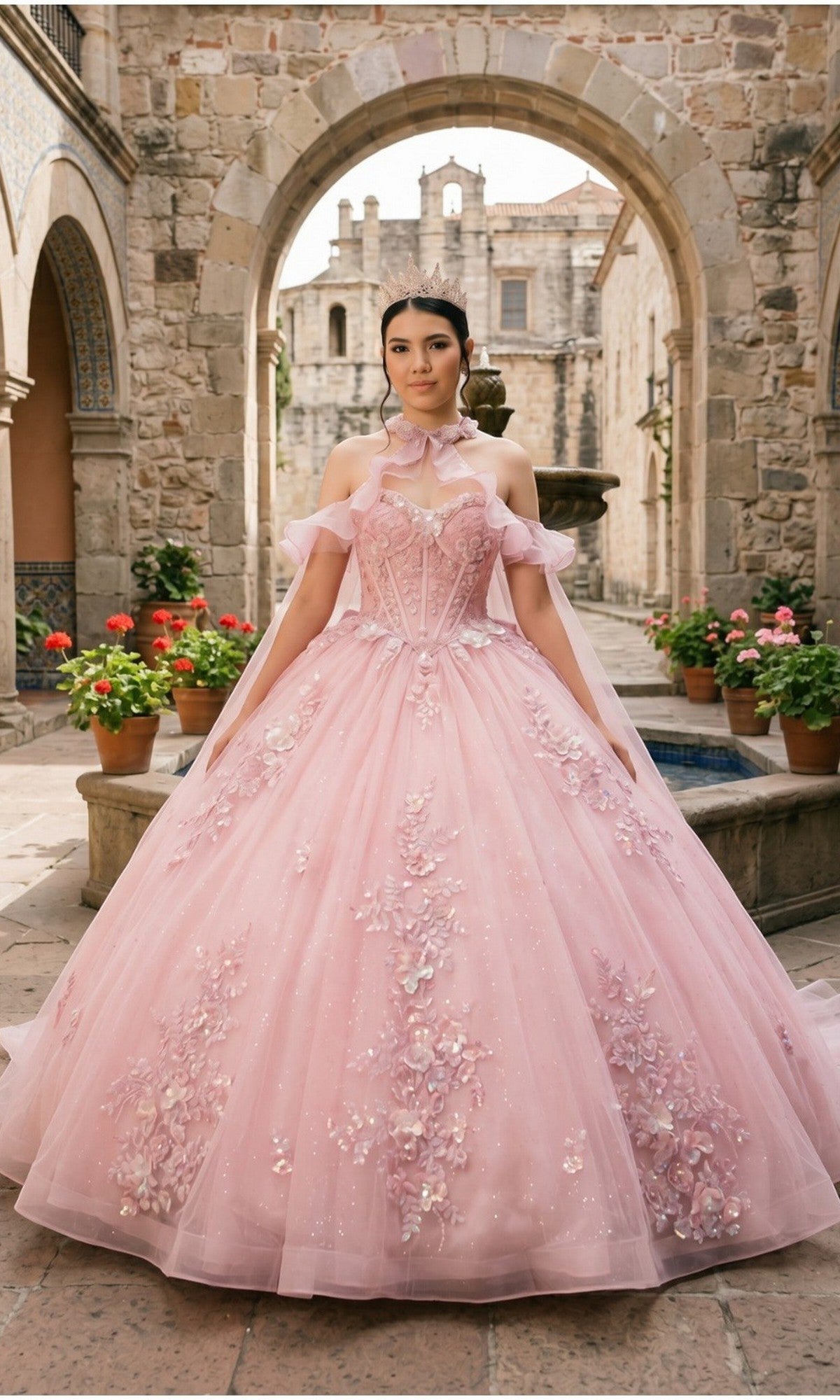 A young woman stands in a stone courtyard with potted plants and arched architecture, wearing the Quinceanera Dress 8585JQ By Cinderella Couture in pink. The gown features a delicate floral lace corset and flows into a shimmering glitter tulle skirt.
